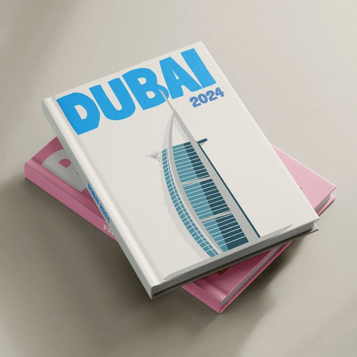 Two Kito travel books stacked on a pale surface — a white DUBAI 2024 cover with an illustrated Burj Al Arab, resting on a pink Paris book.