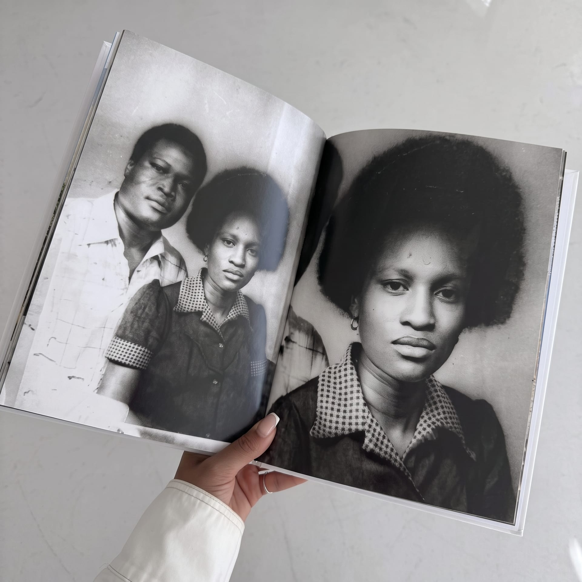 A hand holding open a Kito book at a spread of black-and-white family portraits from the 1970s.
