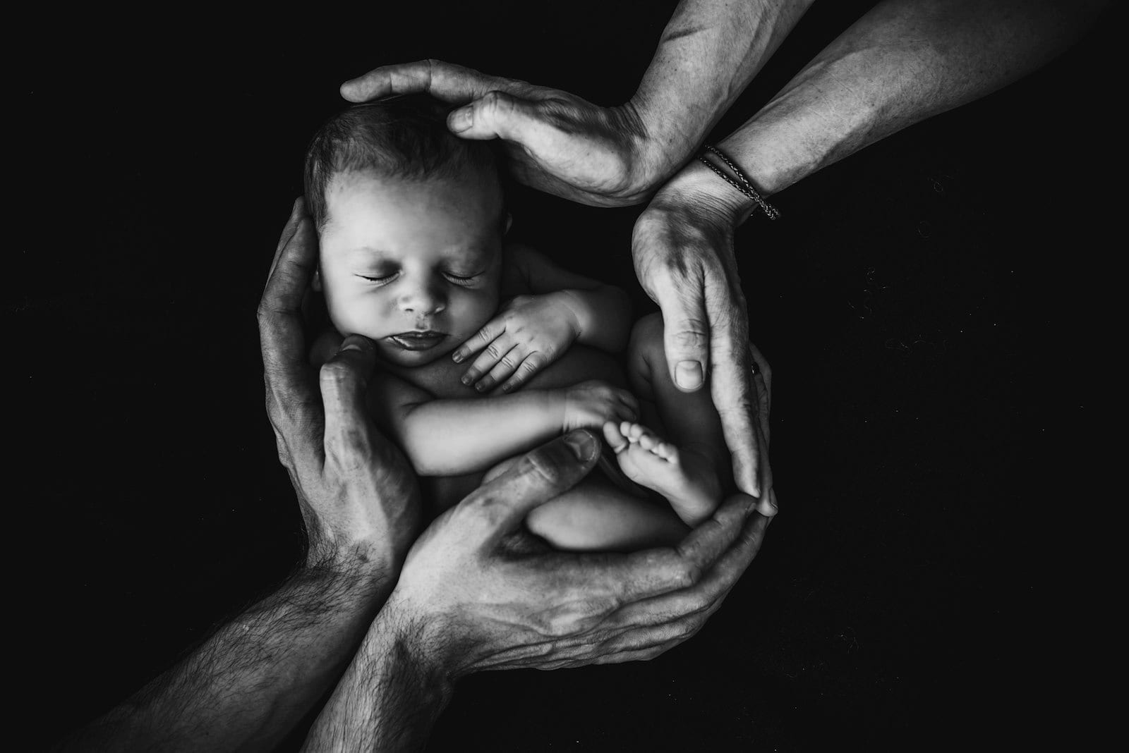 A newborn cradled against a parent's chest in soft black and white.
